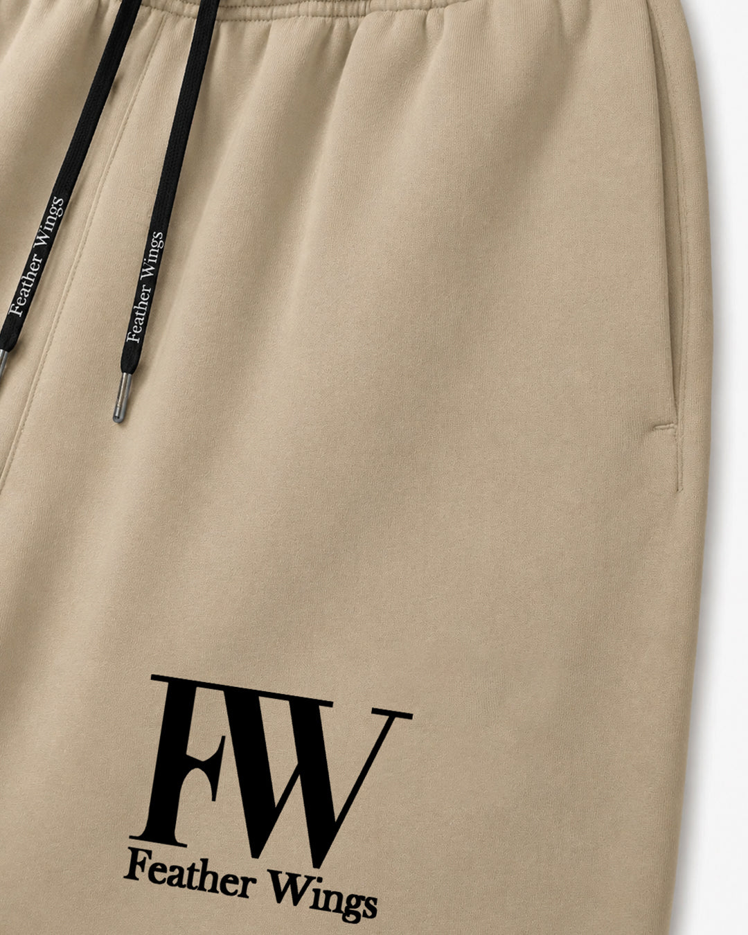Close-up of beige drawstring sweatpants with black drawstrings and a black 'FW Feather Wings' logo printed on the lower left leg.