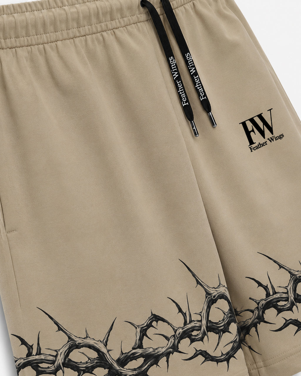 Close-up of beige shorts with black drawstrings, a black FW logo on the left thigh, and a black thorny graphic along the bottom hem.