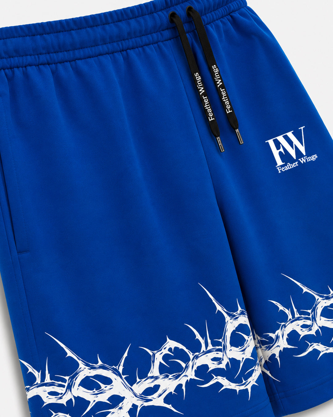 Close-up of royal blue athletic shorts with black drawstrings, a white 'FW Feather Wings' logo on the left thigh, and a white thorny graphic pattern along the lower hem.
