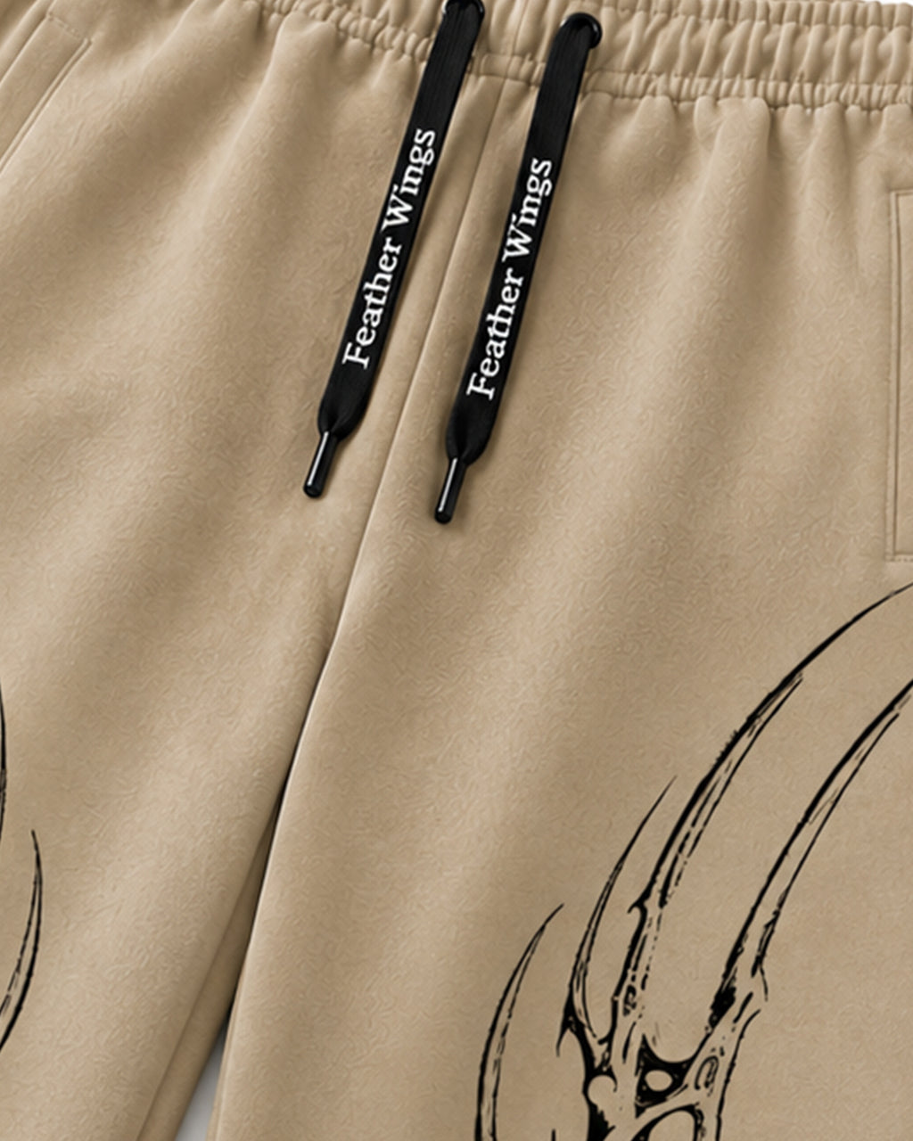 Close-up of beige drawstring pants with black drawstrings printed with 'Feather Wings' and a black graphic design on the leg.