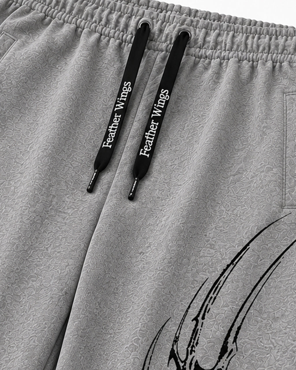 Close-up of light gray heathered sweatpants with black drawstrings printed with the white text 'Feather Wings' and a black graphic near the lower right leg.