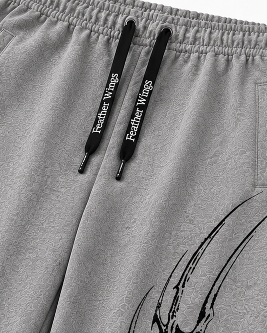Close-up of light gray heathered sweatpants with black drawstrings printed with the white text 'Feather Wings' and a black graphic near the lower right leg.
