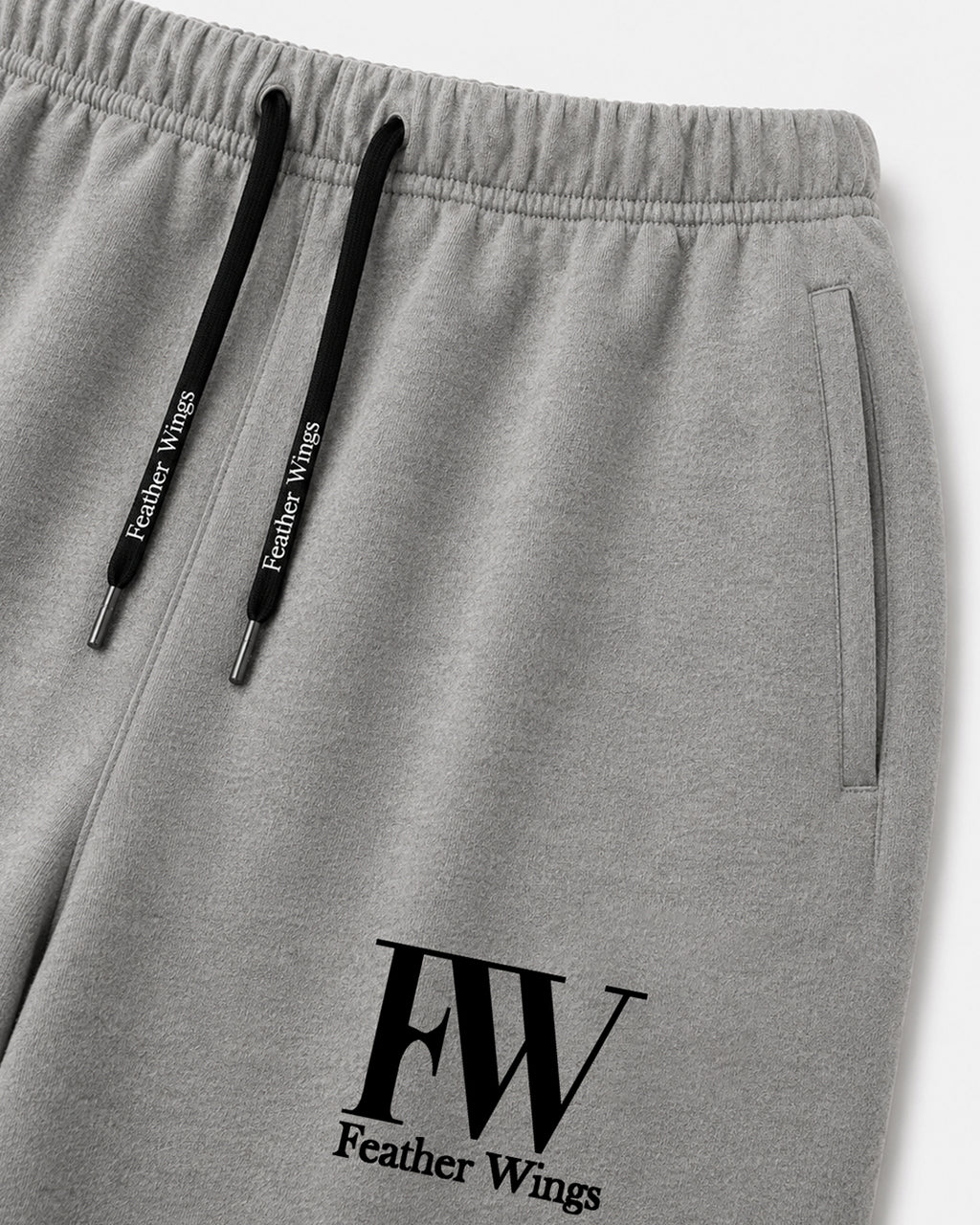 Close-up of gray heather sweatpants with black drawstrings and a black FW Feather Wings logo printed near the lower left leg.