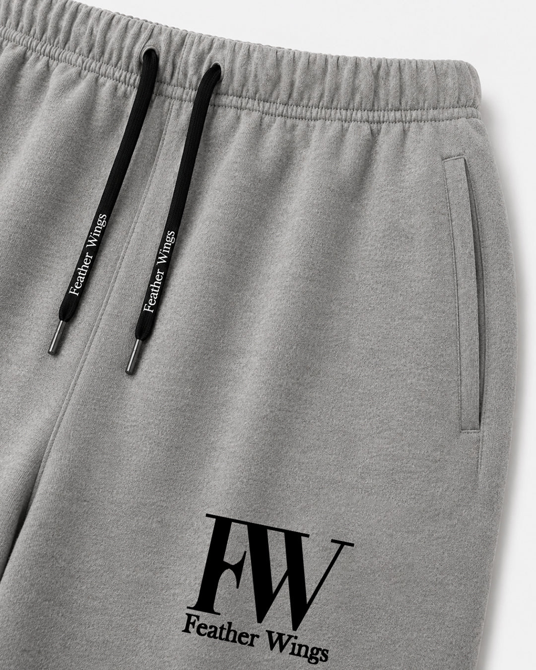 Close-up of gray heather sweatpants with black drawstrings and a black FW Feather Wings logo printed near the lower left leg.